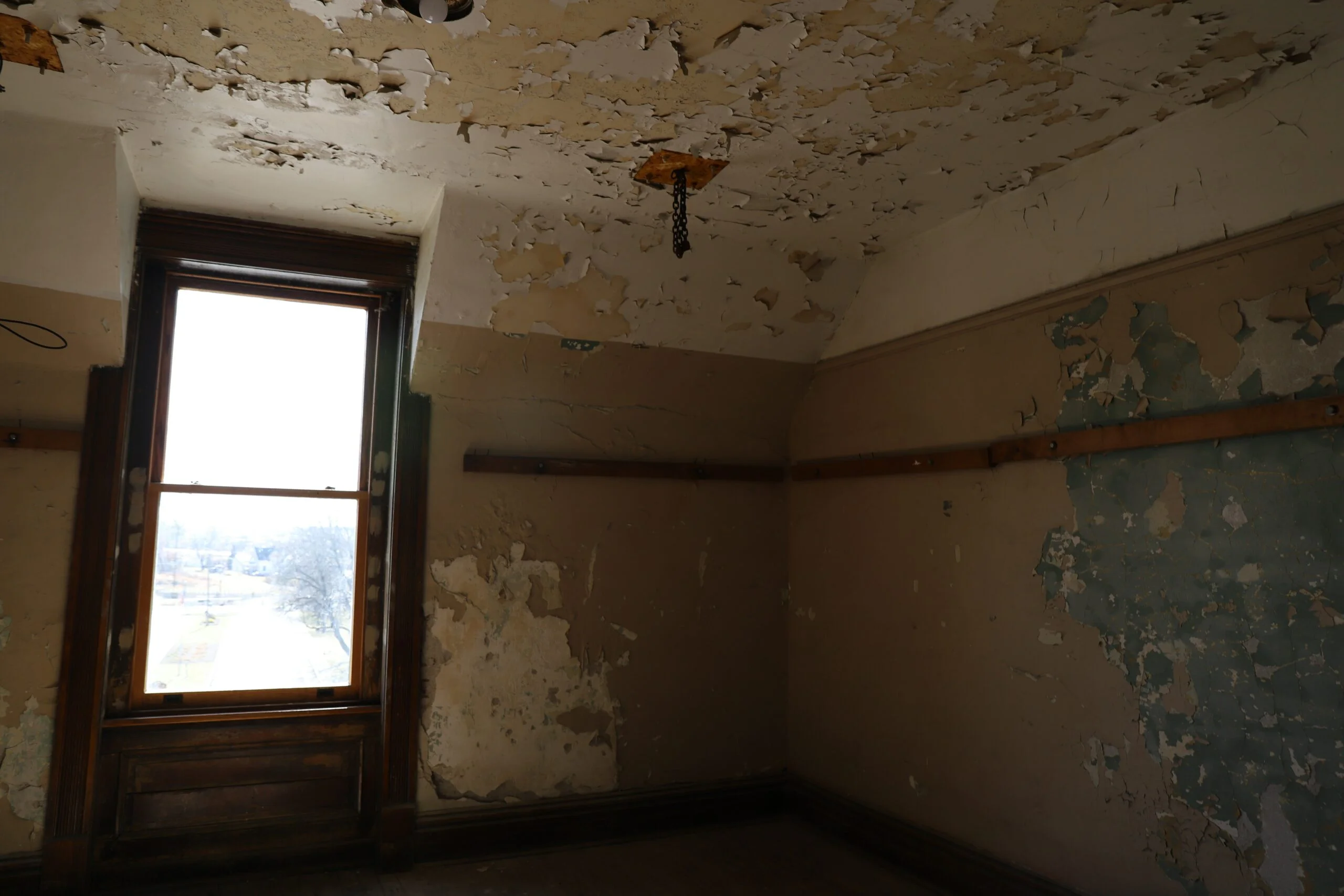 an empty room with peeling paint and a window